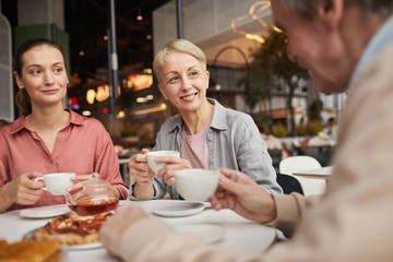 Family of three sitting at the table drinking tea and enjoying each other in cafe
