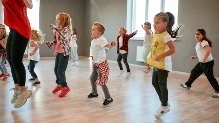 Gordijnen Vol energie. Groep kleine jongens en meisjes die dansen terwijl ze choreografieles hebben in de dansstudio. Vrouwelijke dansleraar en kinderen © Svitlana