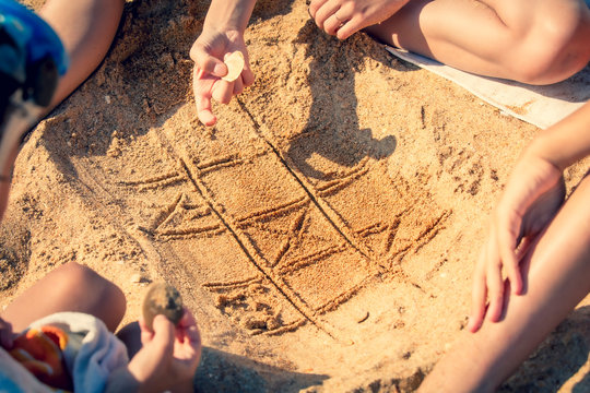 tic tac toe game or X O game write on sand. Fun and games on the sandy beach. Children's hand draws a shell on the sand - Powered by Adobe