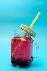 A refreshing drink of berries and lemon in a glass with a cap on a blue background