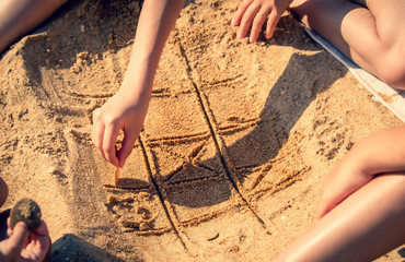 tic tac toe game or X O game write on sand. Fun and games on the sandy beach. Children's hand draws a shell on the sand