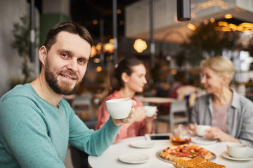 Portrait of young man smiling at camera and drinking tea with his family during lunch