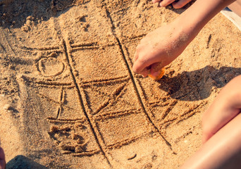 tic tac toe game or X O game write on sand. Fun and games on the sandy beach. Children's hand draws a shell on the sand