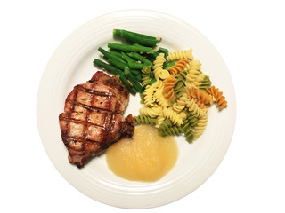 A grilled Pork Loin Chop on a plate with green beans and almonds, tri-color rotini pasta and applesauce.