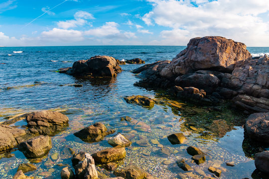 rocky shoreline of the sea in the morning. beautiful scenery with splashing waves and clouds on the sky. calm summer weather