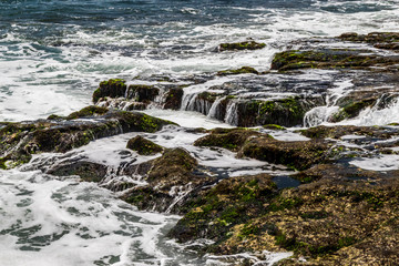 Ocean water flowing over rocks exposed at low tide; Bali, Indonesia. 
