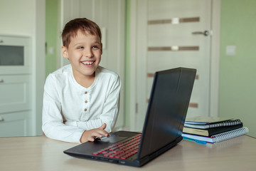 Fototapeta premium home electronic distance learning. Cute happy child doing homework at home using a laptop. covid-19 epidemic and pandemic education