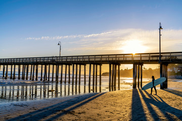 Surfer Walking by Pier at Sunset 