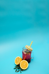 A refreshing drink of berries and lemon in a glass with a cap on a blue background