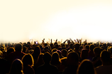 crowd with raised hands at a concert of a music festival. Silhouettes of people in front of a stage...