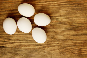 Five white chicken eggs on brown wooden table, horizontal view.  Abstract food background. 