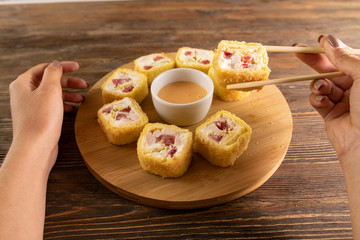 hand hold fried sushi roll with salmon, tomato and sauce on wooden circle board