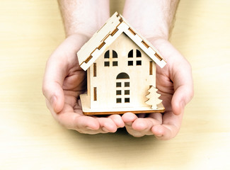 A small wooden house in male hands. The concept of buying, selling, renting real estate. Happiness at home
