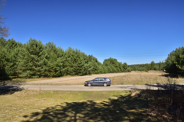 Obraz na płótnie Canvas Samochód kombi na drodze w lesie na tle niebieskiego nieba.