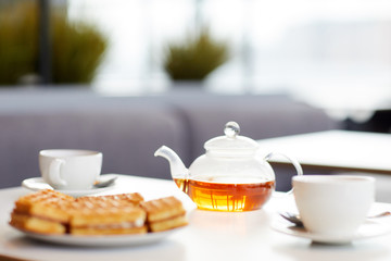 Image of teapot with cups and cakes are on the table prepared for breakfast in cafe