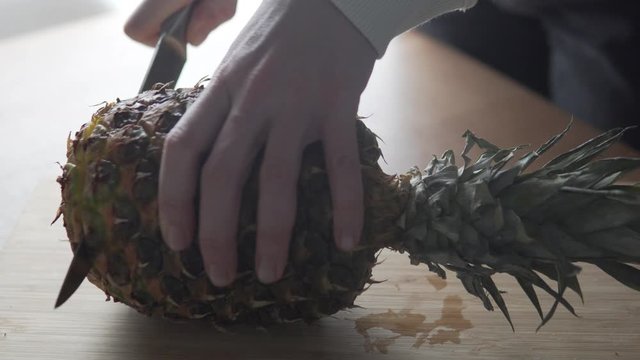 A large pineapple is cut with a knife in the kitchen.