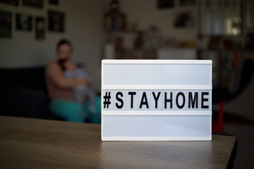 Little girl playing at home with some wooden blocks in front of a sign saying to #stayhome