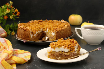 Cake with apples, meringues and cup of tea is located on a plate on a dark background
