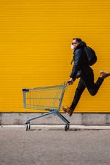 Man with a protective mask in a hurry runs with a shopping cart to the store.