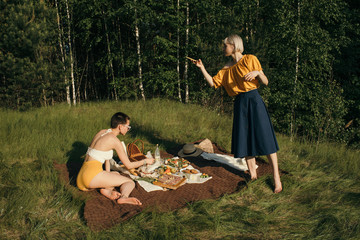 Girlfriends resting on meadow during picnic in forest