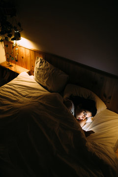 Girl looking her mobile phone in bed at night.