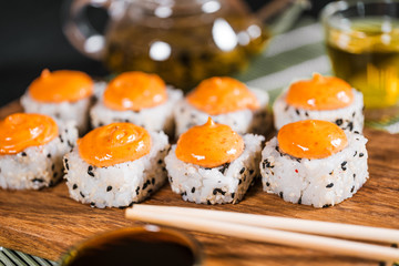 Delicious rolls with spicy sauce on wooden board. Close up of tasty sushi rolls.