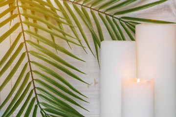 Palm branches and white pillar candles on a white wooden background.
