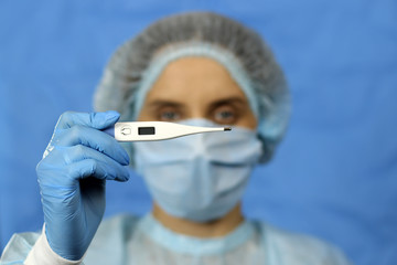 young woman doctor nurse in a coat and hat with a thermometer in hand on a blue background,...