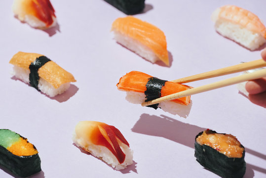 Assorted sushi set with chopsticks on pink background.