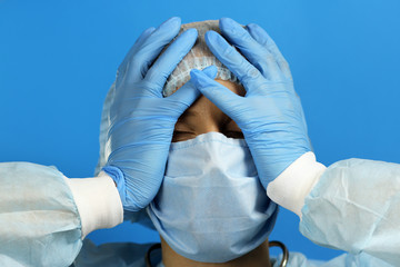 Fototapeta premium Attractive female doctor in a dressing gown , medical mask is upset, in a panic holding her hands to head