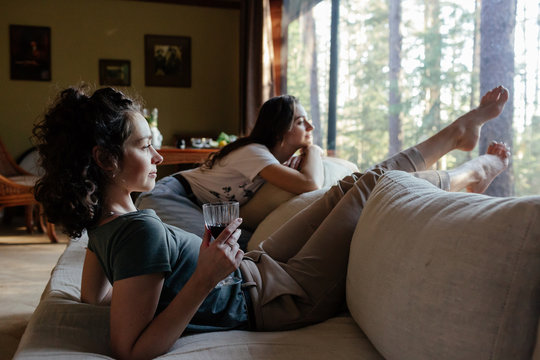 Young women looking through window while sitting on sofa at home