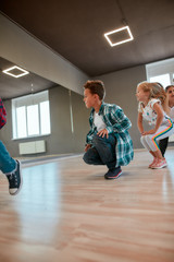 Warming up. Little active boys and girls in casual clothes doing squats in the dance studio. Children warming up before dance class