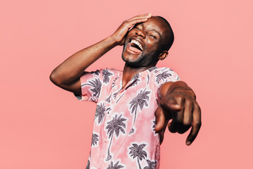 Happy young black man laughing at pointing at camera with finger over pink background