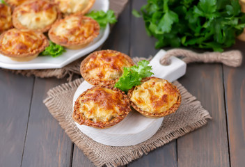 Pastry tartlets with mushrooms and chicken on a wooden board. Rustic background, selective focus. 