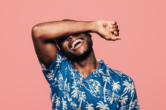 Portrait of black man covering his face with arm over light pink background