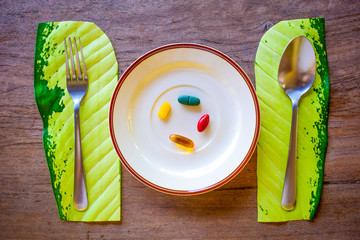 Vitamin pills served with spoon and fork in plate on the wooden table. Omega 3 pill, multi vitamin...