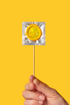 Female hand with condom packing on stick.