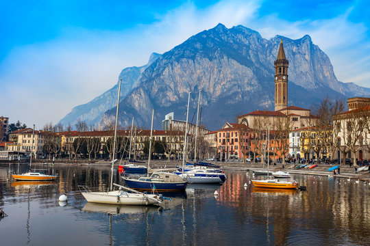 Lecco, Italy, February 16, 2020. The picturesque embankment of Lake Como in cloudy weather and the mountains behind it. Boats are reflected in the water