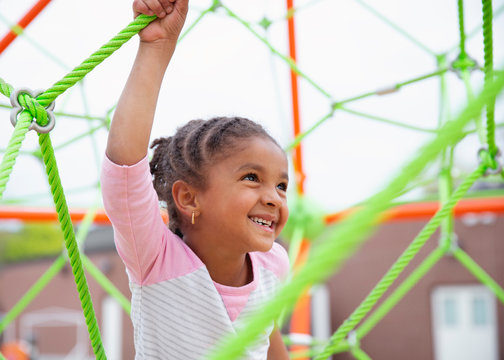 Closeup Portrait of a young child with braids in her hair climbing a spider string type structure at a playground