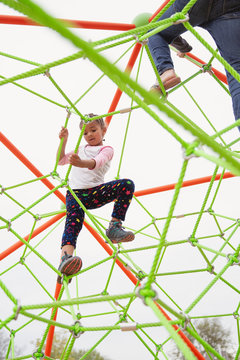 Young child with braids in her hair climbing a spider string type structure at a playground with her sister