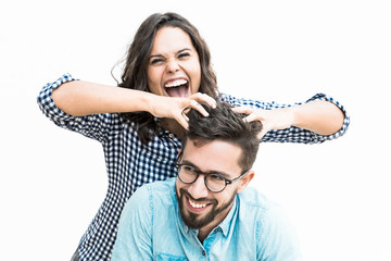 Excited joyful woman setting funny hair of her happy boyfriend. Young woman in casual and man in glasses standing isolated over white background. Fun and joy together concept