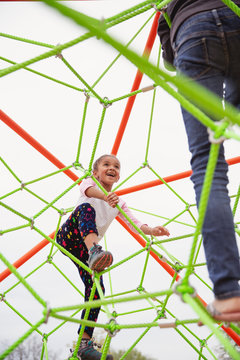 Young child with braids in her hair climbing a spider string type structure at a playground with her sister