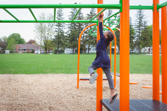 Young mixed child jumping onto the monkey bars at a playground