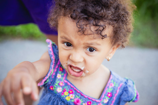 Closeup portrait of an angry pointing child with messy icecream around her mouth.
