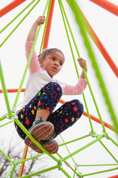 Young child with braids in her hair climbing a spider string type structure at a playground