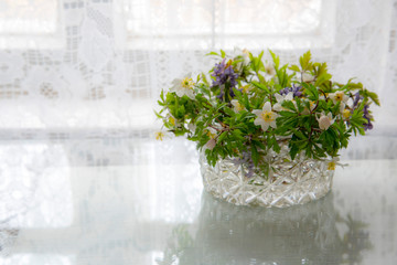 A crystal vase with forest flowers on a background of lace curtains.