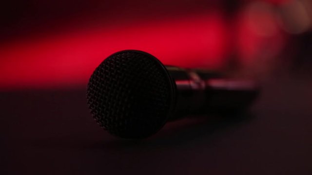 The microphone lies on the stage against the background of a concert show, performance or karaoke. Dynamic background color bokeh. The concept of a musical instrument.
