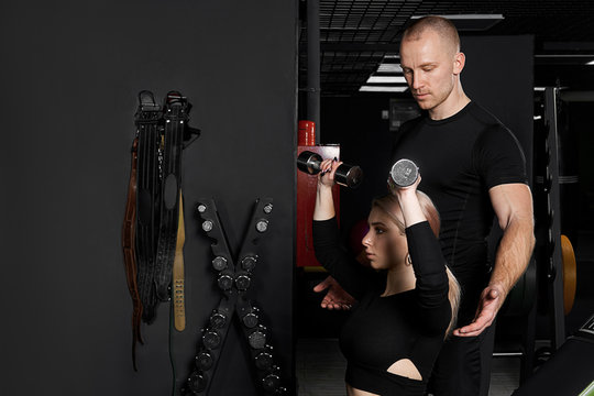 Coach is showing woman how to train in gym to lose weight. Dumbbell lifting with instructor.