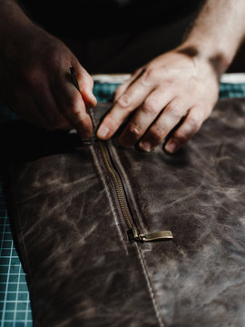 Detail of a handmade process: man makes a product (bag) from leather and makes a zip.