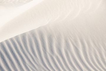 Obraz premium Beautiful beach background. Sand, wave, reflect, shadow, light, beige. Patterns in sand of dune like ruffle in water.